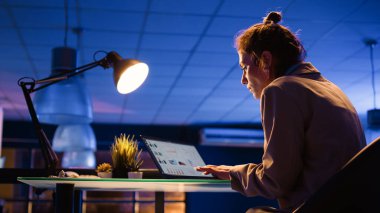 Corporate employee analyzing financial report with diagrams and graphs, planning business investment. Young woman working on development with marketing analytics. Handheld shot.