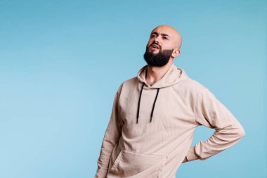 Genç Arap adam omurga sorunları yaşarken el ele tutuşuyor. Sırt ağrısı ve ağrılı kramplardan muzdaripken yukarı bakan sakallı bir insan.