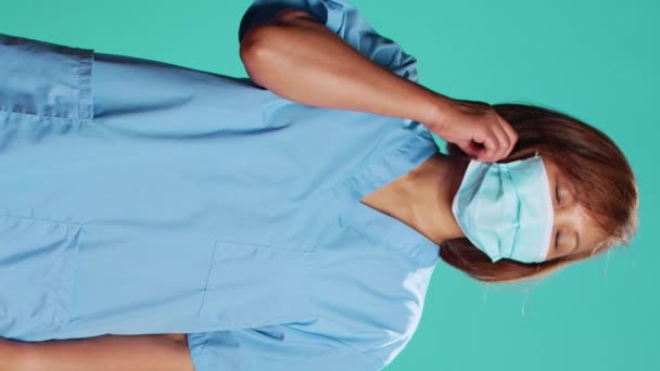 劳累的护士下班后摘下防护面罩 亚洲诊所的员工很高兴终于摘下了令人窒息的卫生巾 隔离在蓝色的工作室背景下 — 图库视频影像