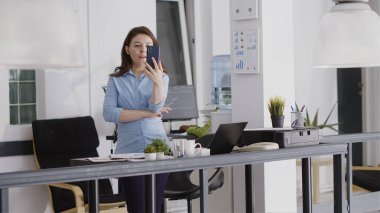 Ajans çalışanı akıllı telefondan video görüşmesi yapıyor. İnternetteki telekonferans görüşmesinde iş arkadaşlarıyla konuşuyor. Genç girişimci profesyonel ofiste uzaktan kumandayla konuşuyor..