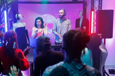 Gece kulübü partisinde canlı performans sergilerken sahnede çalan bir grup. Kalabalık dans ediyor ve dans pistinde ritme ayak uyduruyor. Kulüpteki şarkıcı ve DJ elektronik müzik konserinde.