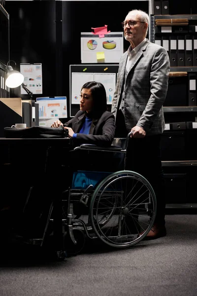 휠체어를 일하는 마비된 사업가와 꽃꽂이로 둘러싸인 사무실에서 일하는 동료들 사업장들로 — 스톡 사진