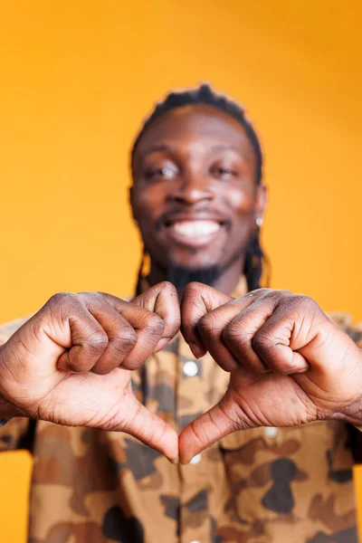 素敵なアフリカ系アメリカ人の男性は 黄色の背景にスタジオで手でハートの形をして ロマンチックなジェスチャーを作ります 愛情と感情を示す陽気な正の人 愛のサインを行う — ストック写真