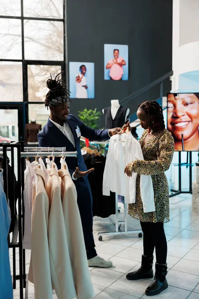 現代のブティックで妊産婦の服のための妊娠中の女性のショッピング 労働者は 右のシャツでクライアントを支援 アフリカ系アメリカ人の顧客が衣料品店でファッショナブルな商品を購入 — ストック写真