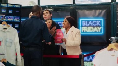 Sabırsız müşteriler, Kara Cuma satışları için sırada bekliyorlar, güvenlik görevlilerini zorluyorlar ve en iyi fiyatları almak için giyim mağazasına giriyorlar. Alışveriş merkezine girmeye zorlayan takıntılı müşteriler.