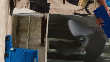 Dikey video yeteneği olan elektrikçi dış klima iç bileşenlerini tamir ediyor, freon seviyesini kontrol ediyor ve termostatları ayarlıyor. Afrika kökenli Amerikalı tamirci bakım planına bakıyor.