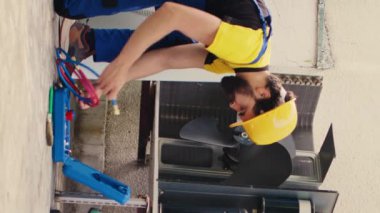 Dikey video elektrikçisi yıllık hvac sistem araştırması yapıyor, yoğunlaştırıcıya monte etmeden önce manifold göstergelerini birleştiriyor. Uzman tamirci soğutucu sızıntısı arıyor. Bu da soğutma sisteminin zayıflamasına yol açıyor.