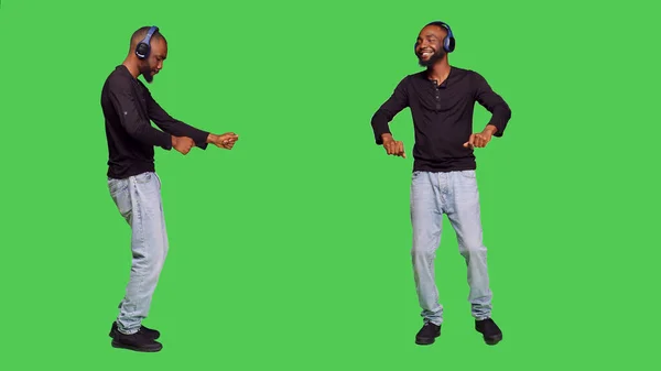 カメラで踊るヘッドフォンを持つ男性モデル オーディオヘッドセット上の音楽を聞いて 楽しみを持っています 緑の画面の上に立って 彼が肯定的な歌を楽しんでいる間にダンスの動きをする若い人 — ストック写真