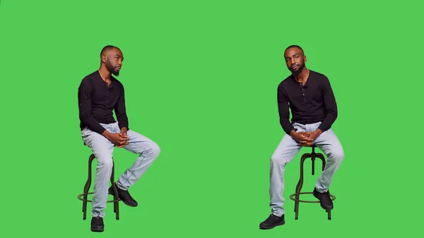 アフリカ系アメリカ人の男性の椅子に自信を持ってポーズを取り フルボディの緑の画面の背景に座っている 若い男性モデルは楽観的に感じ スタジオで何かを待っています 自然人 — ストック写真