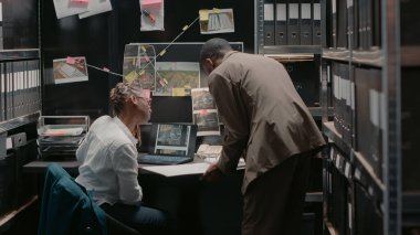 African american law agents working with case evidence on papers and laptop, reading statements and doing background checks. Two private detectives examining criminal records. Handheld shot.