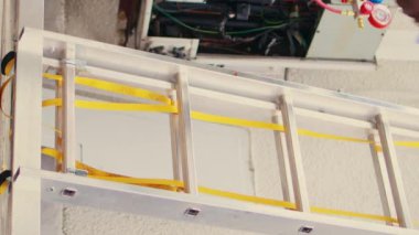 Becerikli elektrikçinin el matkabı tutarak çatı kaplama sisteminin bakımını yapmak için merdivene tırmandığı dikey video zemin görüntüsü. Deneyimli bir kablocu, yoğunlaştırıcıyı kontrol etmek için görevlendirildi.