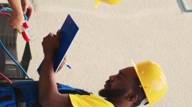 Dikey video Deneyimli Tamirci kondansatör araştırmaları, filtre değişiklikleri ve gerekli düzeltmeler yaparken HVAC sistem arızalarını önlemek için usta tamirci bulguları panoya yazarken