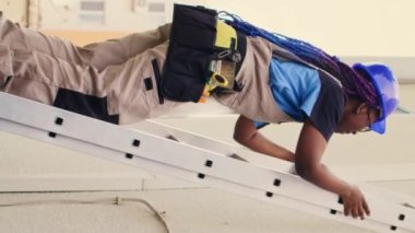 Elektrikli matkabı tutan dikey video uzmanı çatı hvac sisteminin bakımını bitirdikten sonra merdivenden iniyor. Havada araştırma yapmak için görevlendirilmiş bilgili bir profesyonel.