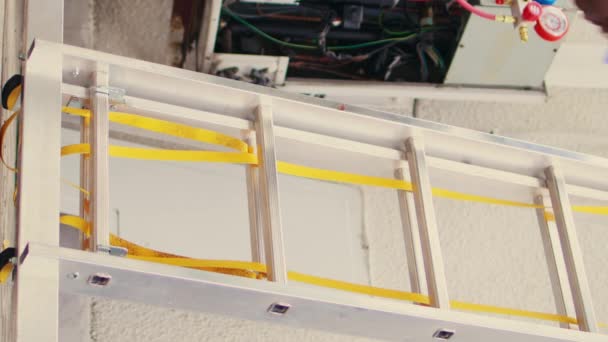 垂直ビデオ屋上のHvacシステムのメンテナンスを行うには 手ドリルクライミング折り畳みはしごを保持する能力のある電気技師の地上レベルのショット コンデンサの点検を委託された季節の女性 — ストック動画