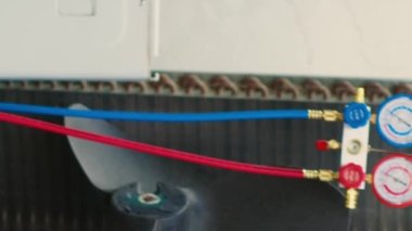 Dikey video nitelikli elektrikçi, kondansatör açmak ve manifold göstergelerini bağlamak için el matkabı kullanarak bozuk klima üzerinde çalışmaya başlıyor. İşçi basınç ölçmeye başlamak için hvac sistemi açıyor