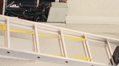 Elektrikli matkabı tutan dikey video uzmanı çatıdaki hvac sistemini tamir ettikten sonra merdivenden inerken iş arkadaşı freonu kontrol etmek için manifold göstergelerini birleştiriyor.