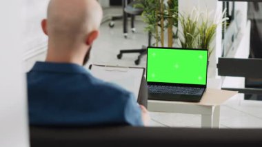 Yeşil ekran görüntüleme belgelerini inceleyen şirket çalışanı, açık alandaki kromakey boş şablona bakıyor. Başarılı araştırma planı için dizüstü bilgisayar ve analiz kullanan iş adamı.