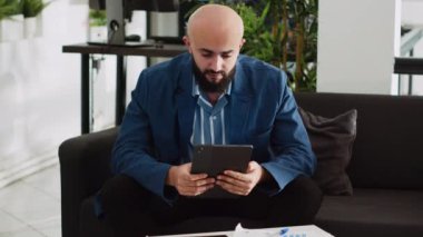 Tabletteki şirket sorunlarını çözen iş adamı, açık uzay ofisindeki online istatistiklere ya da analizlere bakıyor. Girişimci başarılı bir yazılım geliştiriyor, başlangıç planı üzerinde çalışıyor. El kamerasıyla..