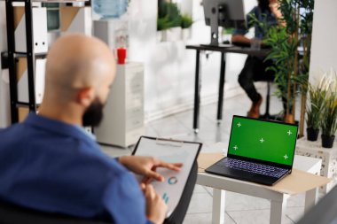 Krom ekranlı dizüstü bilgisayarda çalışan ve ortak çalışma alanındaki finansal verileri kontrol eden bir iş adamı. İş ofisinde yeşil ekranlı taşınabilir bilgisayar kullanan yönetici