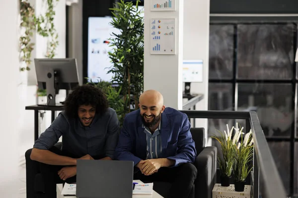 兴奋的Arab员工一边坐在沙发上一边在笔记本电脑上一边检查成功的营销活动 两名企业家在商业机构分析财务报告 — 图库照片
