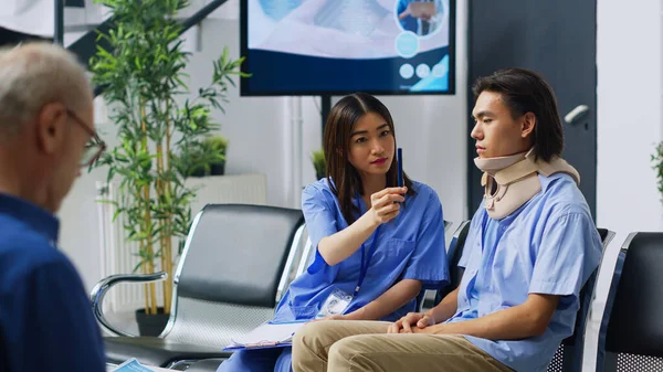アジアの看護師は 患者の目のビジョンをチェックし 病院のレセプションでの協議中に医療の専門知識を議論 首の事故後子宮頸部の襟を身に着けている負傷者 医療サポートを受けます — ストック写真