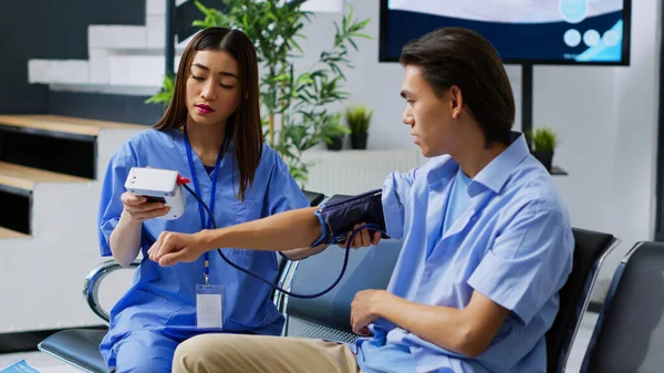 病気の人の高血圧と血圧を測定するアシスタントは 病院のロビーでの訪問相談中にメートル法で心臓検査を行う 看護師コンサルティングアジア人患者医療支援 — ストック写真