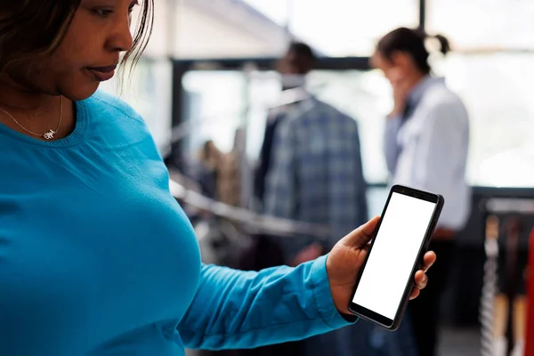 アフリカ系アメリカ人の顧客は ショッピングモール内のブランクスクリーンで携帯電話を保持し ファッションストアアプリをチェックする おしゃれな女性がファッショナブルな商品を購入し モックアップディスプレイでスマートフォンをチェック — ストック写真