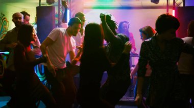Kutlamada dans eden gülümseyen insanlar modern müzik dinliyorlar, dans pistinde parti yapıyorlar. Farklı yetişkinler DJ 'lerle ve sahne ışıklarıyla eğleniyor. El kamerasıyla..