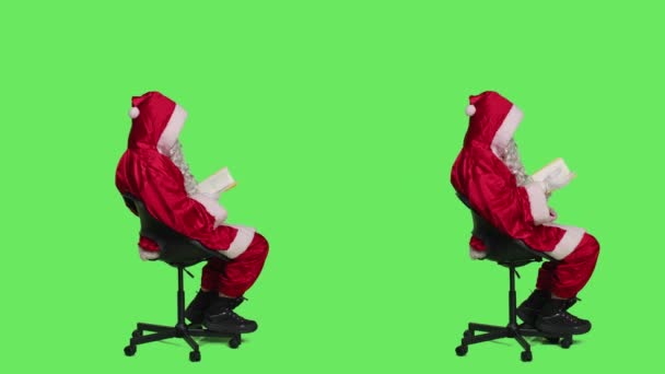 キャラクターは椅子に座って有名な赤いスーツで聖人ニックのような演技小説の物語の本を読み取ります 緑の画面の背景 父のクリスマスの読書文学や詩を描いた若い男 賢明な人 — ストック動画
