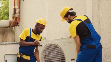 Teamworking diverse specialists starting work on damaged hvac system, taking apart condenser coil panel. Skilled wiremen dismantling air conditioner to check for bad wiring clipart