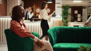 Mutlu gülümseyen turist portresi modern otel salonunda oturuyor. Tatilde rahat bir turist lobide oturuyor, bir oda verilmesini bekliyor, kapatıyorlar.