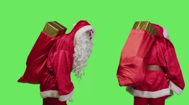Yetişkin aziz Nick çocuklar için hediyelerle dolu kırmızı çuval taşır, Noel arifesi ruhunu temsil etmek için beyaz sakallı mevsimlik kostüm giyer. Çantalı Noel Baba yeşil perde arkaplanının üstünde.