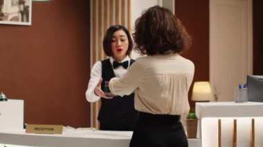 Otel müdürü, turist konaklama belgelerinin dosyalarını neşeli resepsiyoniste veriyor. Mutlu gülümseyen profesyonel personel şık bir dinlenme odasında çalışıyor.