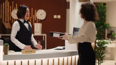 Gülümseyen otel müdürü mutlu resepsiyonistlere seyahat rezervasyonlarının dosyalarını veriyor. Modern otel lobisinde çalışan neşeli profesyonel personel..