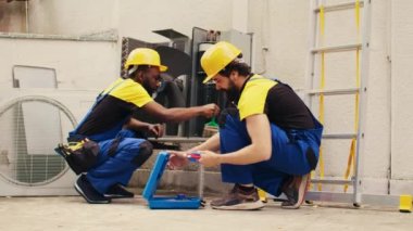 İş arkadaşı Hvac sistemindeki freon seviyelerini kontrol etmek için profesyonel manifold göstergelerini birleştirirken Afro-Amerikan servis elemanı tozun havalandırma iç bileşenlerini temizliyor