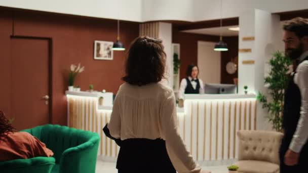 在酒店办理入住手续的女商人 在行李服务员的帮助下 接待员检查订房详情 由随行人员协助的专业旅行度假者 — 图库视频影像