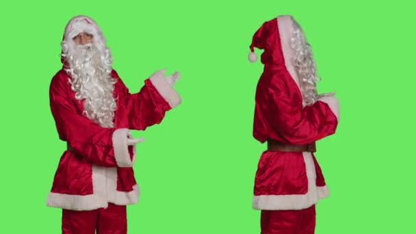 父親のクリスマス広告何か 彼はスタンタクラスのお祝いの衣装と緑の画面の背景に立っている間脇を指して 聖人ニックのような服を着た男 Xmasマーケティングキャンペーン — ストック動画