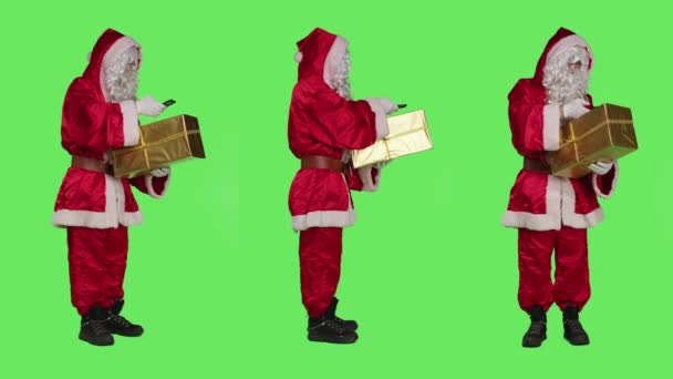 圣诞老人在全身绿屏的背景下拍摄礼物盒的照片 在送礼物给孩子们之前检查礼物 年轻男子圣徒尼克字符与智能手机和包装 — 图库视频影像
