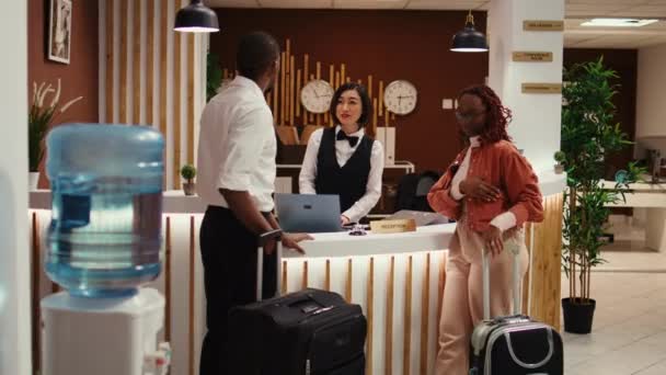 アフリカ系アメリカ人のカップルにポッシュホテルで休暇パッケージのオプションを提示フレンドリーな受付 新婚旅行で夫と妻リゾートラウンジで余分な部屋のアメニティを支払う準備 — ストック動画