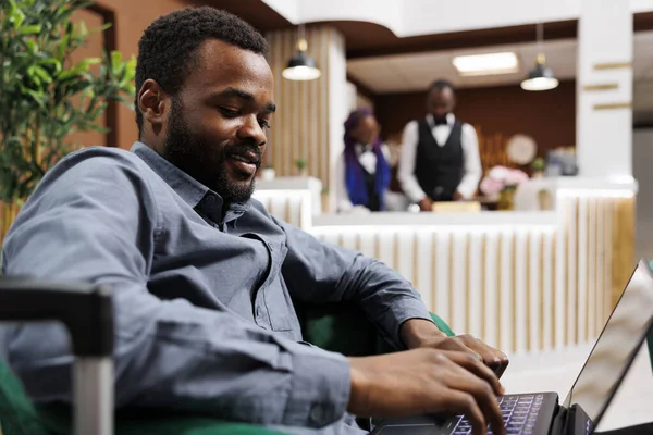 Usmívající Mladý Afroameričan Muž Podnikatel Pomocí Notebooku Zatímco Čeká Kufrem — Stock fotografie