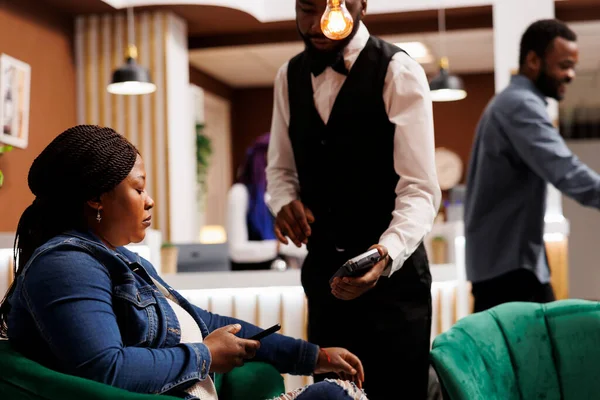 Afroamerykanin Kelner Hotelowy Trzymający Terminal Pos Otrzymujący Płatność Bezgotówkową Kobiety — Zdjęcie stockowe