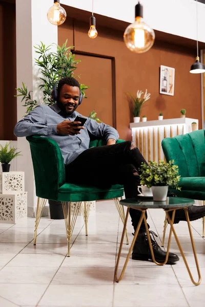Smiling African American Man Wearing Wireless Headphones Relaxing Hotel Lobby — Stock Photo, Image