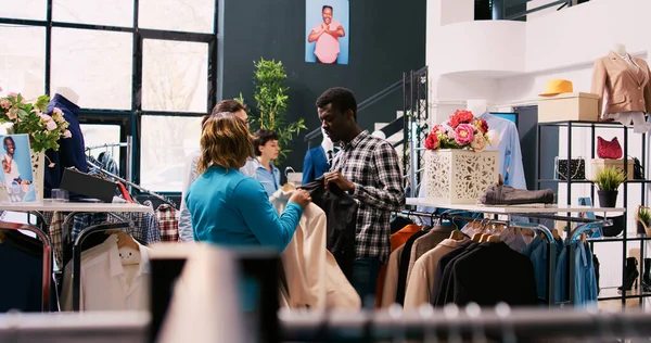 アジアのスタイリッシュな従業員は モダンなブティックで商品生地を議論し 正式な衣装でカップルを支援します アフリカ系アメリカ人のお客様 服店でファッショナブルな服を買う — ストック写真