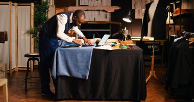 Tebeşirle el işi yaparak terzilik atölyesinde moda koleksiyonu tasarlamak için kumaş işaretleyen genç bir terzi. Tasarımcı tasarımcı. Lüks giysi yapımı, işçiliği üzerine çalışıyor..