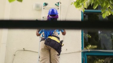 Elinde elektrikli matkap tutan usta bir tamirci çatıdaki havalandırma sistemini kontrol ettikten sonra merdivenden iniyor. Bakım görevinin sonunda iyi bir işçi.