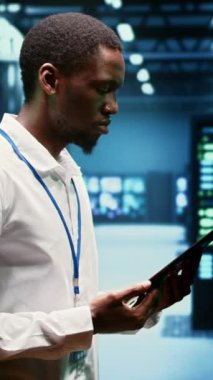 Dikey video deneyimli bilgisayar bilimcisi sunucu satırlarını maintenaning web içeriğini çevrimiçi müşterilere dağıtıyor. Kritik sistemlerin işlevselliğini sağlamak için tablet kullanan Afrikalı Amerikalı denetçi