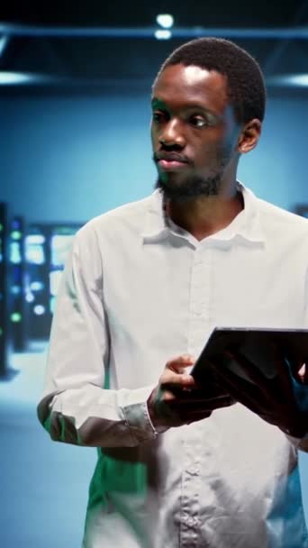 垂直ビデオアフリカ系アメリカ人技術者は 膨大なコンピューティングリソースを提供するハイテク施設にスーパーコンピュータ ストレージデバイス ネットワーク部品を収容しています サーバーの専門家 — ストック動画