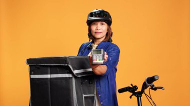 Kurye müşterilere sipariş edilen yiyeceklerin parasını ödemeleri için POS satın almayı teklif ediyor. Başarılı teslimattan sonra NFC ödeme seçeneği sunan Asyalı kadın, turuncu stüdyo arka planında izole edilmiş