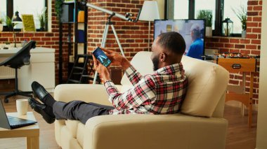 Mutlu oyuncu akıllı telefondan jiroskop kullanarak uzay gemisi uçuş oyunu oynuyor. Heyecanlı, rahat, rekabetçi bir adam güzel, rahat bir apartman dairesinde eğleniyor.