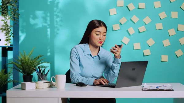 Businesswoman adding card information, managing payment method on laptop while at work. Asian employee sitting at colourful bright modern office desk over blue studio background